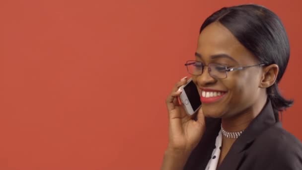 Bastante mujer de negocios habla en el iPhone sentado delante de la pared roja — Vídeos de Stock