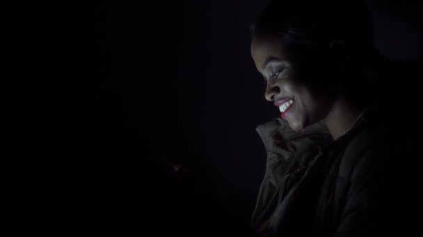 Черная женщина дергает свой телефон в темноте — стоковое видео
