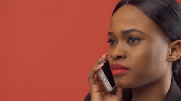 Mulher negra bate-papo com alguém via iPhone sentado diante da parede vermelha — Vídeo de Stock