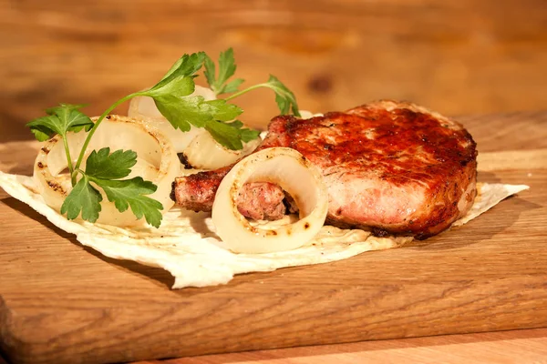 Zusammensetzung aus saftigen Stück gegrilltem Fleisch, Zwiebeln und Kräutern und Fladenbrot auf einem Holzbrett. — Stockfoto
