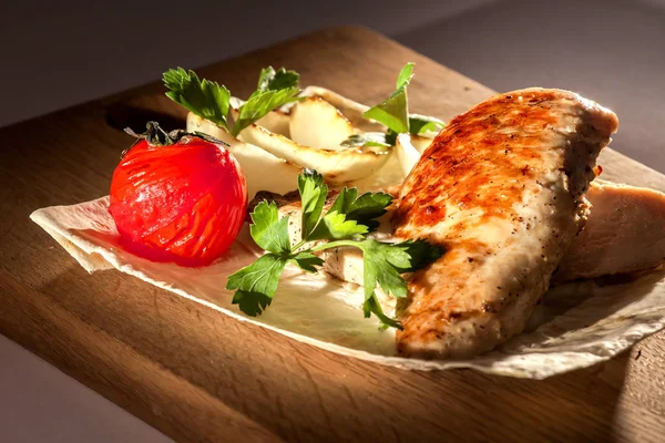 Grilled chicken fillet on a pita bread with grilled tomato, onion and herbs. Food on a wooden board.
