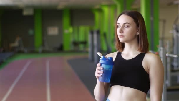 Sportwoman jest woda pitna z niebieskie plastikowe butelki po ciężkich treningów na siłowni — Wideo stockowe
