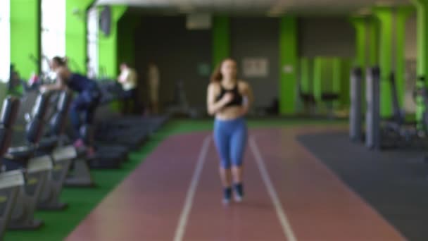 La mujer horizontal borrosa con el tatuaje corriendo en el gimnasio verde — Vídeos de Stock