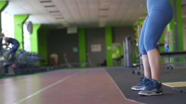 El retrato lateral cerrado de la deportista en pantalones azules luciendo el kettlebell en el gimnasio verde — Vídeo de stock