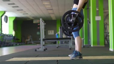 Yukarı kaldırarak ve halter Mavi pantolon yeşil spor salonunda genç kadın tarafından aşağı koyarak. Yakın çekim manzara fotoğraf