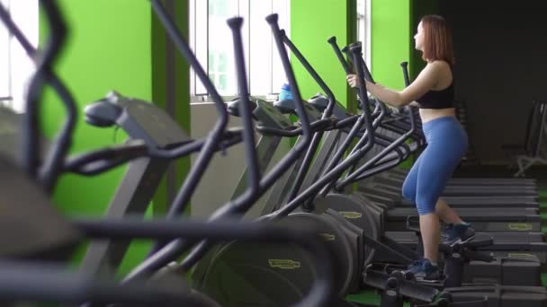 Sportwoman in de zwarte top en blauw broek doen oefeningen op de trainer van de stap te houden fit en haar beenspieren trainen. — Stockvideo