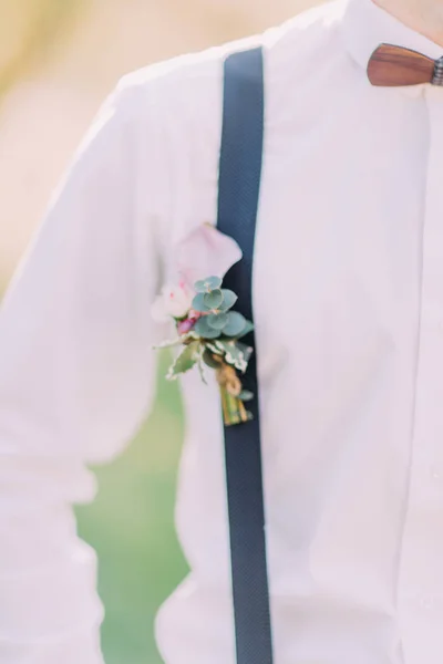 La foto de cerca lateral de la perspectiva del novio en la camisa de mierda, mariposa de madera y tirante con los accesorios de flores en el fondo del campo de primavera verde . — Foto de Stock