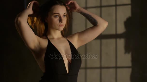 The close-up portrait of the woman in the black swimsuit sorting and holding the hair at the dark background. — Stock Video