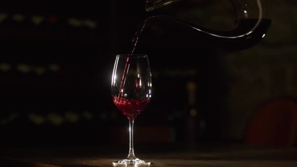 Το χέρι που ρίχνει το κόκκινο κρασί από καράφα σε το wineglass στο σκούρο φόντο. — Αρχείο Βίντεο