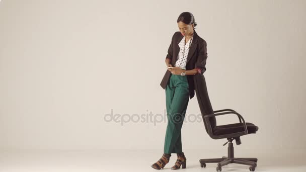 Black business lady writes something in her iPhone leaning on office chair — Stock Video