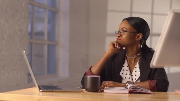 Занятая черная женщина снимает очки, сидя за рабочим столом. — стоковое видео