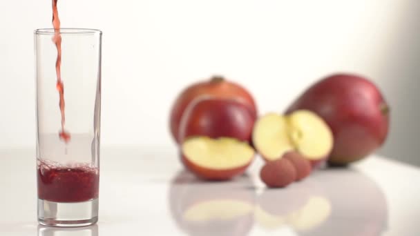 O suco derrama em um copo na mesa com maçãs cortadas — Vídeo de Stock