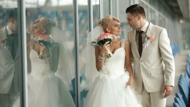 Bruidegom bewondert bruid terwijl ze langs de rijen op voetbalstadion lopen — Stockvideo