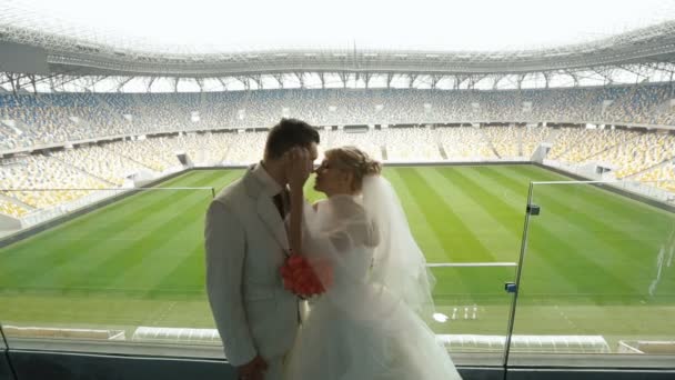 Bride kisses groom on the balcony over football field — Stock Video