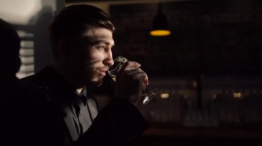 Siyah saçlı siyah takım elbise giyen adamla bira içme ve karanlık pub duvara yaslanmış. Yan yakın çekim portre.