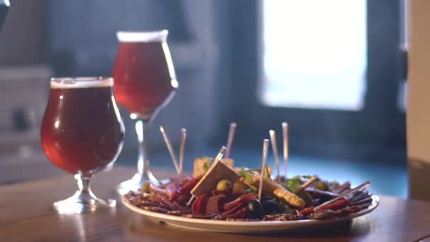 De close-up samenstelling van de plaat vlees en twee glazen met bier, gelegen op de houten tafel in de achtergrond van de kroeg vol met rook. — Stockvideo