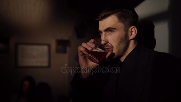 El triste hombre enojado está bebiendo cerveza y ordenando su cabello mientras se apoya en la pared de la barra oscura. El retrato lateral de primer plano . — Vídeos de Stock