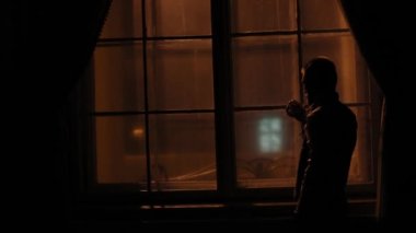 Adam ayakta, karanlık odada viski içme ve pencereden bakarak yakın çekim arka portresi.