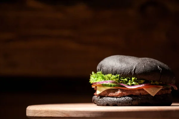 Крупним планом чорний смачний бургер з сиром, салатом та м'ясом на дерев'яній дошці . — стокове фото