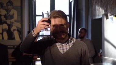 Sakallı mutlu gülümseyen adam barda arkadaşlarının arka plan, bira içiyor onun glassand yetiştirme.