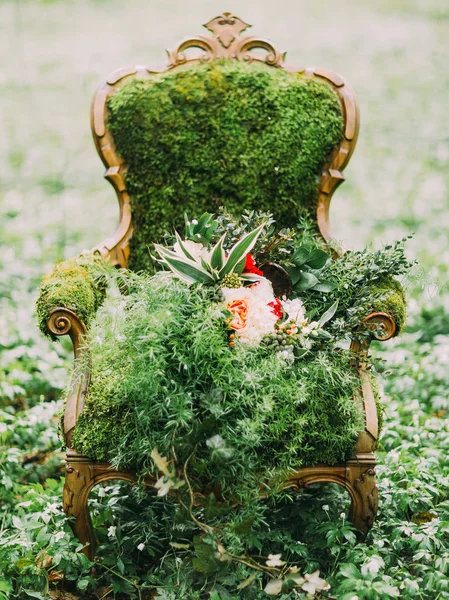 La composición verde. La silla está cubierta con el musgo y el enorme ramo se encuentra sobre ella en la hierba verde . — Foto de Stock
