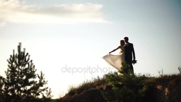 A házaspár newlywed átölelve és megcsókolta a hegyek tetején a naplemente alatt. — Stock videók