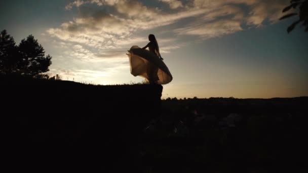 La mariée tourne autour dans sa longue robe de mariée blanche au sommet de la roche pendant le coucher du soleil. Le portrait horizontal .
