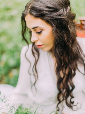 Uzun kıvırcık saç ve kedi gözleri yeşil arka plan yere bakarak kadınla yakın çekim yan portresi.