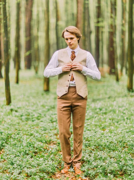 O retrato completo do homem de terno vintage abotoando seu colete e olhando para o chão verde na floresta da primavera . — Fotografia de Stock