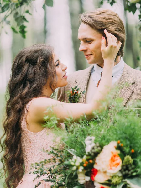 Närbild foto av den vackra bruden med långt lockigt hår är sortering håret av brudgummen håller den stora buketten på bakgrunden till den gröna skogen. — Stockfoto