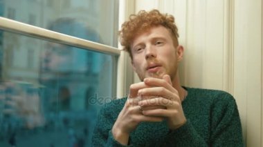 Öksürük ve kafede pencereden bakarak hansome adam sarışın kıvırcık saçlı bir fincan sıcak çay, holding yakın çekim portresi