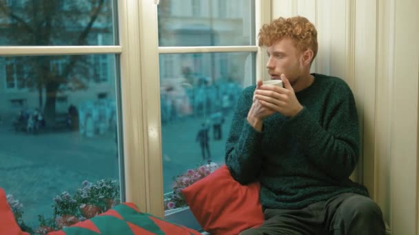 Uomo biondo malato con i capelli ricci che beve tè sul davanzale della caffetteria. Ha il raffreddore. — Video Stock