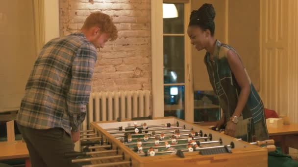아프리카 땋은 최신 유행 옷을 입고 아프리카계 미국 흑인 여자와 골든 곱슬 머리와 수염 잘생긴 남자의 사랑 스러운 커플 흰색 벽돌 벽의 배경에서 테이블 축구를 연주하는 — 비디오