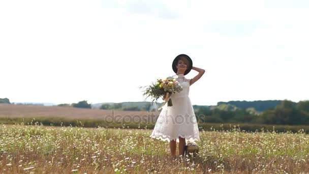 白いヴィンテージのドレスに回転し、日当たりの良いフィールドの背景に美しい花束を保持している美しい女性の水平の肖像. — ストック動画