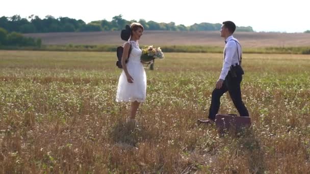 La vue latérale du marié filant la mariée vêtue vintage tenant le bouquet et passant du temps dans le champ ensoleillé . — Video