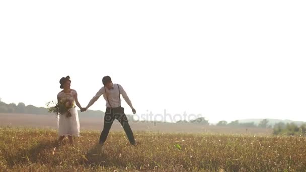 Das alteingesessene Brautpaar hält Händchen und geht durch das sonnige Feld. — Stockvideo