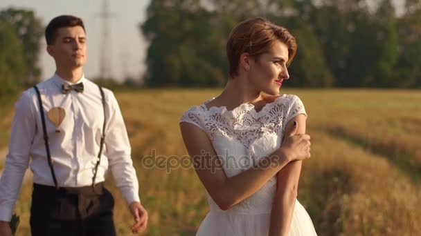 The close-up portrait of the beautiful bride looking at the right side while the groom is hugging her back. The field composition. — Stock Video