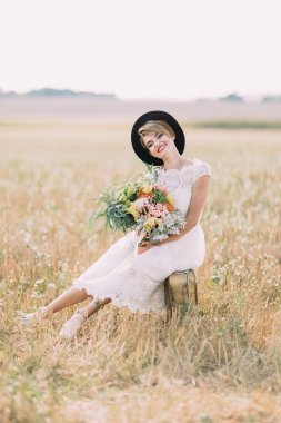 Diz boyu gelinlikle çok güzel gelin renkli buket tutarak ve güneşli alan vintage çantada oturan.