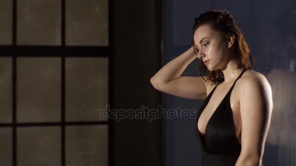 Крупный план бокового портрета мокрой женщины в черном закрытом купальнике, ведущем на стеклянную стену и сортирующим ее короткие влажные волосы . — стоковое видео