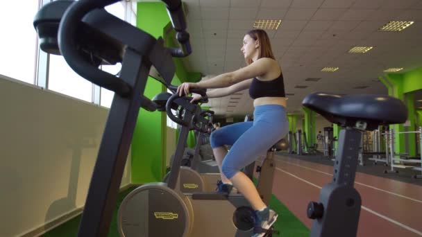 Dół widok kobiety w odzież sportową, uzyskanie kształtu na rower treningowy, w klubie fitness zielony. — Wideo stockowe