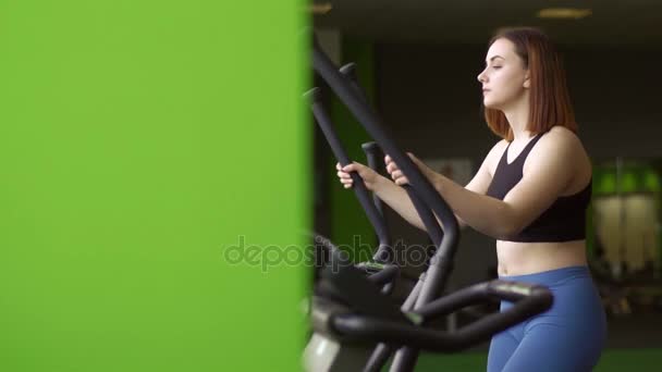 Das seitliche Nahaufnahme-Porträt der Frau, die ihre Muskeln auf dem Ellipsentrainer im grünen Fitnessclub strafft. — Stockvideo