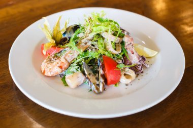 Ahtapot, midye, karides, domates, marul, limon, domates lezzetli deniz ürünleri salatası parmesan peyniri ile dekore edilmiştir. Çanak yan görünüm.