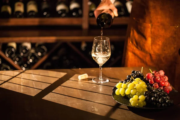 Sommelier gießt Wein in ein Glas. Glas neben Teller mit Früchten. Lage des Weinkellers. — Stockfoto