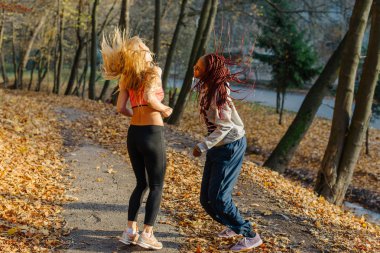 Kızlar autamn Park'ta jogging sonra eğleniyor. Sarışın ve Afrikalı kadınların saç ile oynamak