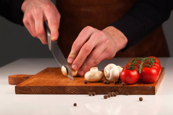 Τα χέρια του σεφ με φέτες μανιτάρια και ντομάτες σε ένα ξύλο κοπής με ένα μεγάλο κοφτερό μαχαίρι — Φωτογραφία Αρχείου