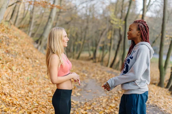 Deux jolies femmes se reposent au parc après avoir fait du jogging. Fille blonde et femme africaine dans le parc d'automne — Photo