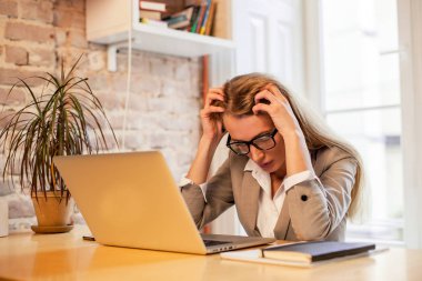 Kafasını tarafından Office elleriyle onu laptop önünde oturan bir bayan. Kadın uzun saçlı ve gözlük.