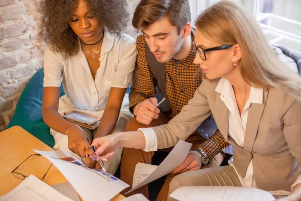 Tres jóvenes empresarios mirando algunos gráficos y discutiéndolos . — Foto de Stock