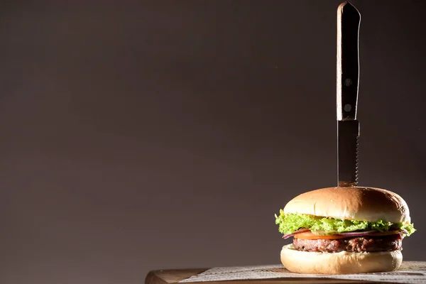 Smaczne, soczyste i świeże burger z sałatką i mięso nożem w nim umieszczone na płycie. — Zdjęcie stockowe