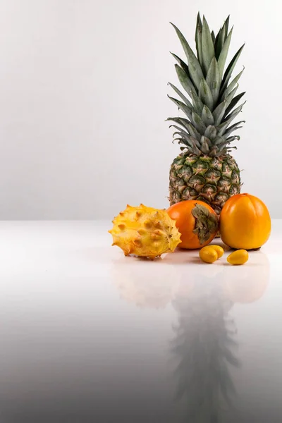 Tiro vertical de composición de frutas tropicales sobre una superficie blanca con reflexión sobre ella — Foto de Stock